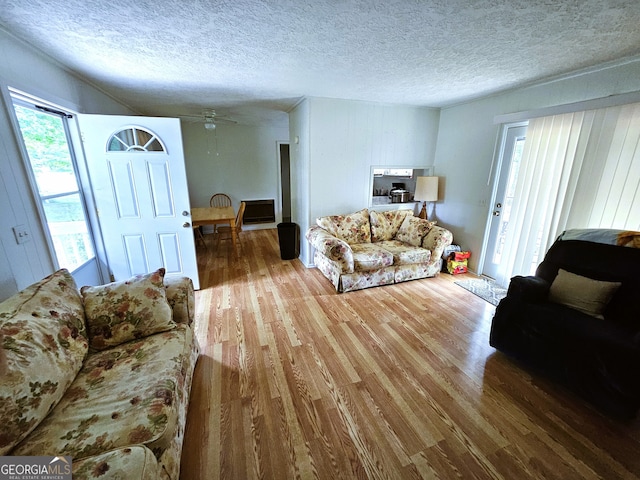 living room with a textured ceiling, ceiling fan, and wood-type flooring