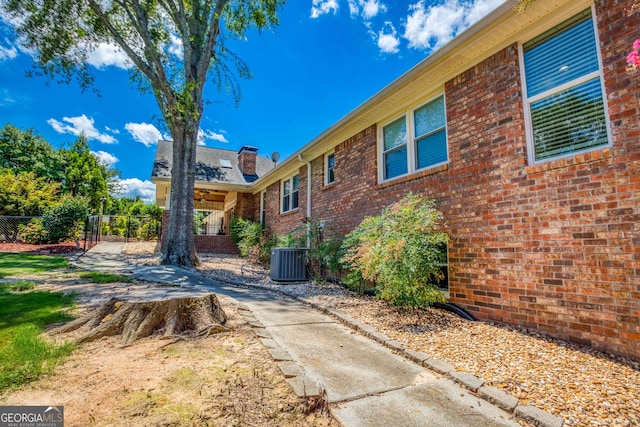 view of home's exterior with brick siding, central AC unit, and fence