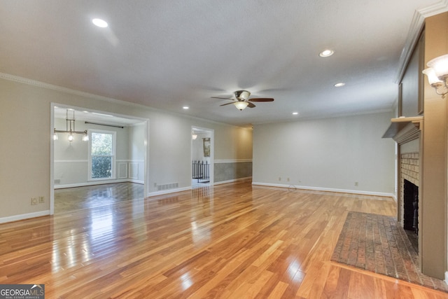 unfurnished living room with crown molding, visible vents, a brick fireplace, light wood-type flooring, and a ceiling fan