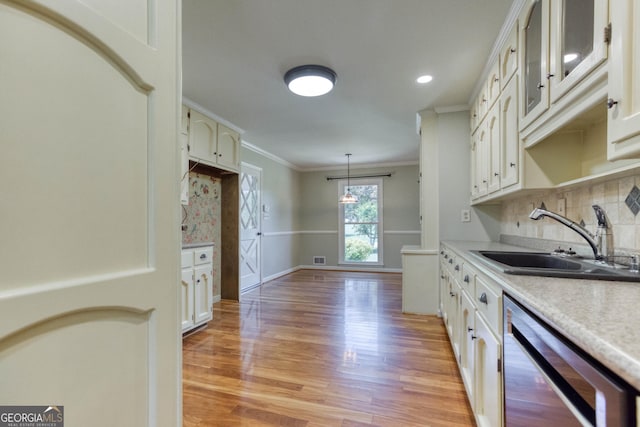 kitchen featuring backsplash, stainless steel dishwasher, a sink, ornamental molding, and light wood-style flooring