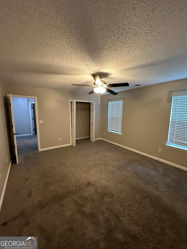 unfurnished bedroom featuring ceiling fan, dark carpet, and a textured ceiling