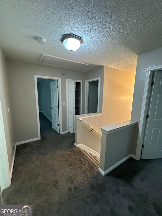 corridor featuring a textured ceiling and dark carpet