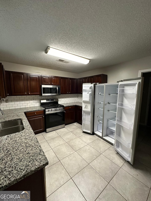 kitchen with light stone countertops, sink, stainless steel appliances, a textured ceiling, and light tile patterned flooring