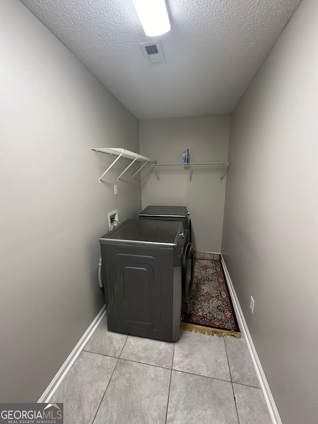 laundry room with washer and clothes dryer, light tile patterned flooring, and a textured ceiling