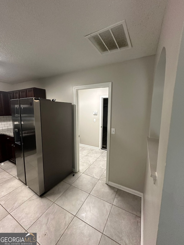 kitchen featuring stainless steel fridge, dark brown cabinets, light tile patterned floors, and light stone counters