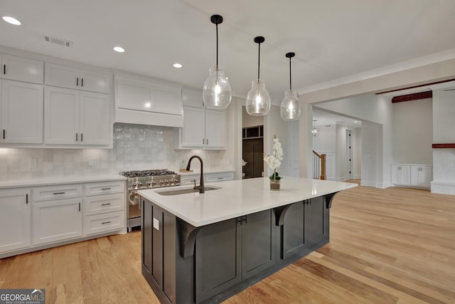 kitchen featuring high end range, hanging light fixtures, white cabinetry, and a center island with sink