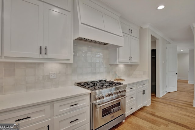 kitchen with custom exhaust hood, white cabinetry, light wood-type flooring, and high end range