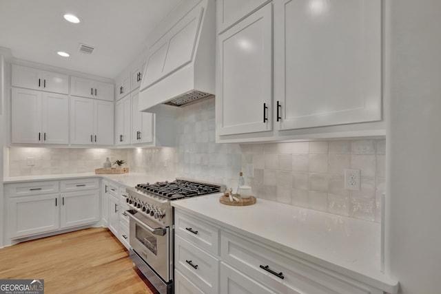 kitchen with light hardwood / wood-style flooring, tasteful backsplash, high end stove, white cabinets, and custom exhaust hood