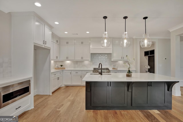 kitchen with stainless steel microwave, white cabinetry, backsplash, hanging light fixtures, and light hardwood / wood-style flooring