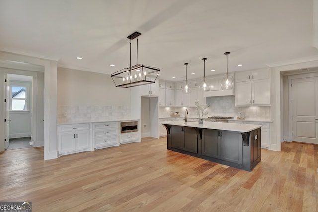 kitchen featuring decorative light fixtures, white cabinetry, an island with sink, sink, and light hardwood / wood-style flooring