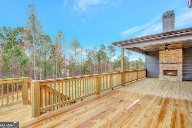 wooden terrace with an outdoor brick fireplace and ceiling fan