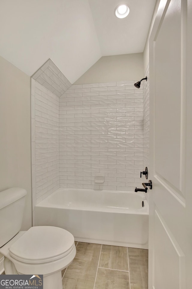 bathroom with tiled shower / bath combo, lofted ceiling, and toilet