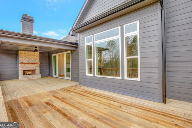 wooden terrace with an outdoor brick fireplace and ceiling fan