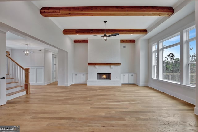 unfurnished living room with ceiling fan, a fireplace, beamed ceiling, and light wood-type flooring