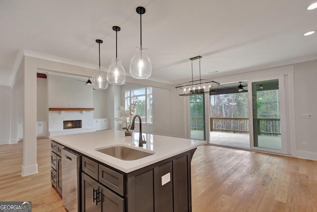 kitchen featuring sink, light hardwood / wood-style flooring, a kitchen island with sink, hanging light fixtures, and stainless steel dishwasher