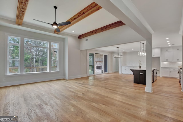 unfurnished living room with ceiling fan with notable chandelier, light hardwood / wood-style flooring, and beamed ceiling