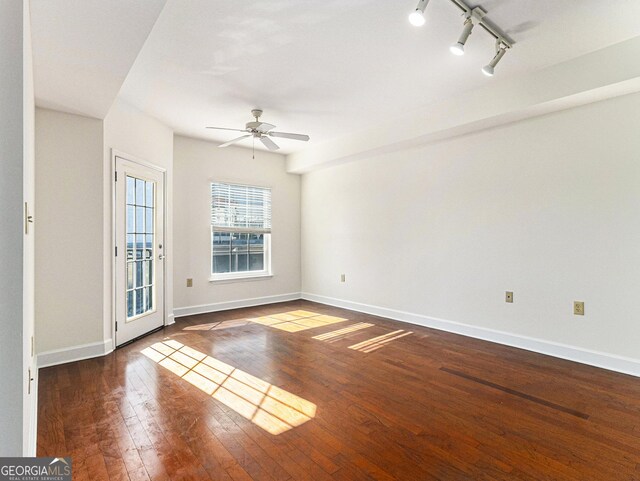 unfurnished room featuring rail lighting, ceiling fan, baseboards, and dark wood-style flooring