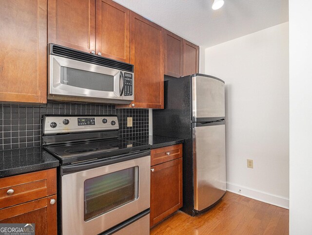 kitchen featuring baseboards, brown cabinetry, appliances with stainless steel finishes, light wood-type flooring, and backsplash