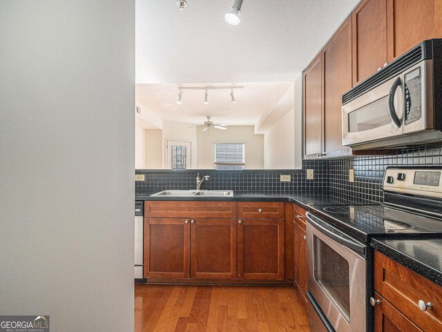 kitchen with appliances with stainless steel finishes, a sink, light wood finished floors, and tasteful backsplash
