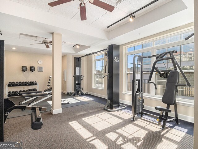 exercise room with baseboards, a raised ceiling, and track lighting