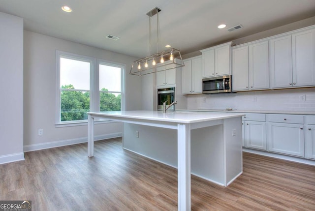 kitchen featuring appliances with stainless steel finishes, hanging light fixtures, a kitchen island with sink, and white cabinets