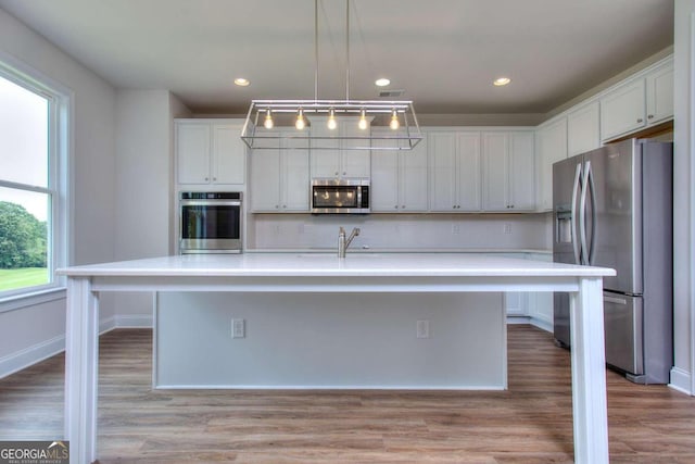 kitchen with a center island with sink, white cabinetry, stainless steel appliances, and decorative light fixtures