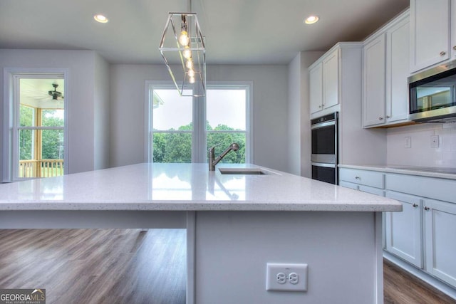 kitchen featuring decorative light fixtures, a kitchen island with sink, appliances with stainless steel finishes, and plenty of natural light