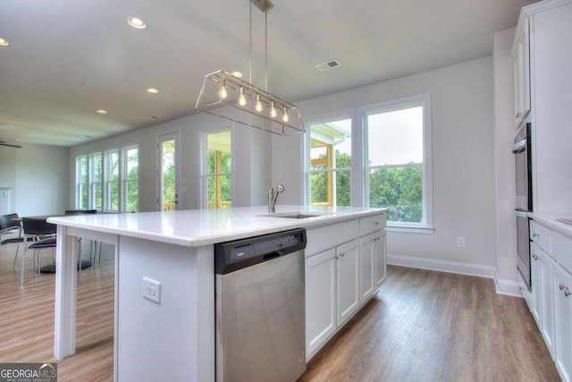 kitchen featuring light wood-type flooring, an island with sink, white cabinets, appliances with stainless steel finishes, and decorative light fixtures