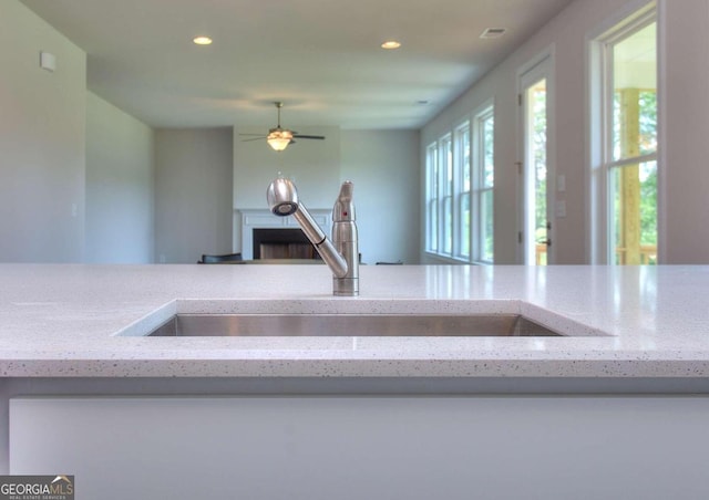 kitchen featuring light stone counters, ceiling fan, and sink