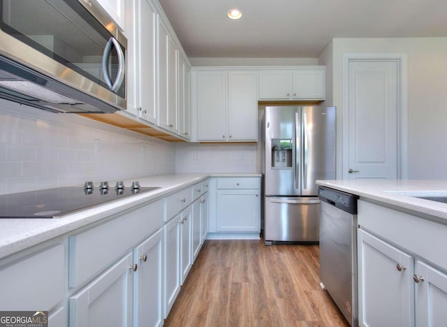 kitchen with light wood-type flooring, light stone counters, white cabinets, backsplash, and appliances with stainless steel finishes