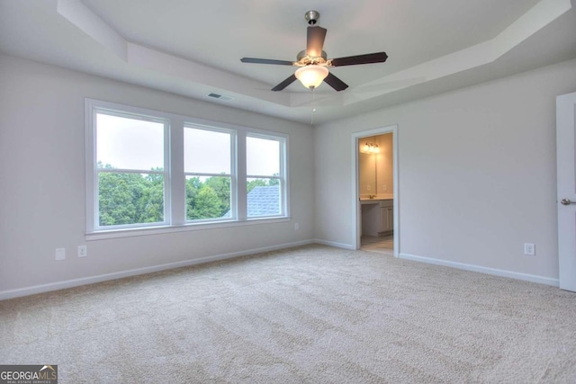 interior space with ceiling fan, a raised ceiling, and ensuite bath