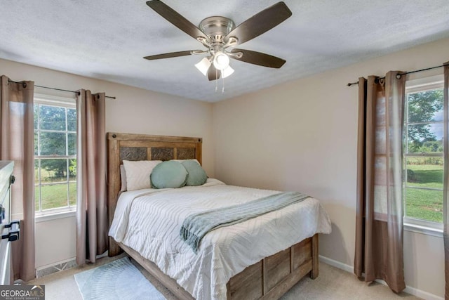 carpeted bedroom featuring a textured ceiling, multiple windows, and ceiling fan