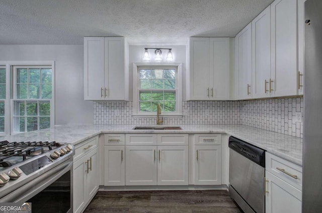 kitchen featuring appliances with stainless steel finishes, white cabinetry, tasteful backsplash, sink, and light stone counters