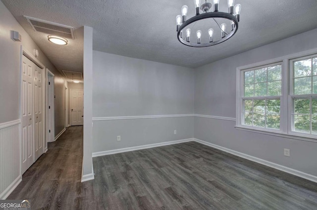 unfurnished room featuring a textured ceiling, dark wood-type flooring, and a notable chandelier