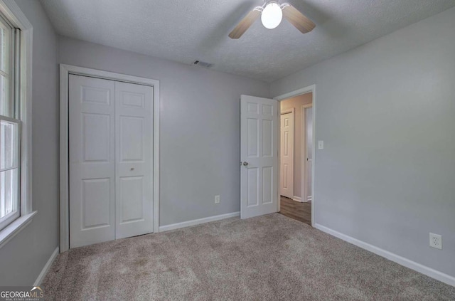 unfurnished bedroom with light carpet, ceiling fan, a closet, and a textured ceiling