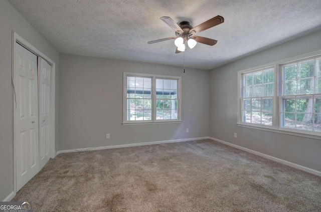 unfurnished bedroom with ceiling fan, light carpet, a closet, and a textured ceiling