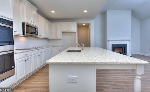 kitchen featuring white cabinets, a sink, appliances with stainless steel finishes, light wood-type flooring, and an island with sink