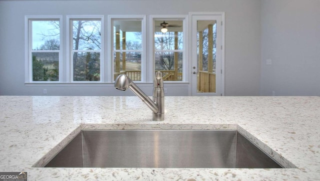 interior details featuring a sink, ceiling fan, and light stone counters