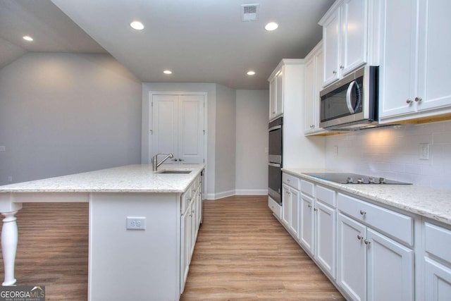 kitchen featuring stainless steel microwave, light wood-style floors, backsplash, a sink, and white cabinetry