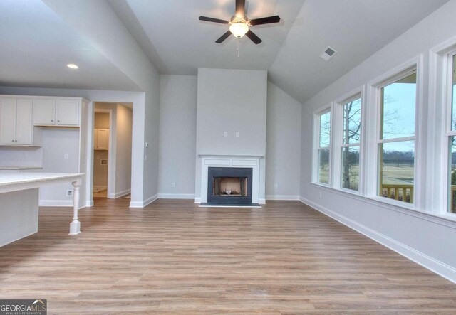 unfurnished living room featuring a fireplace with flush hearth, visible vents, baseboards, light wood-type flooring, and a ceiling fan
