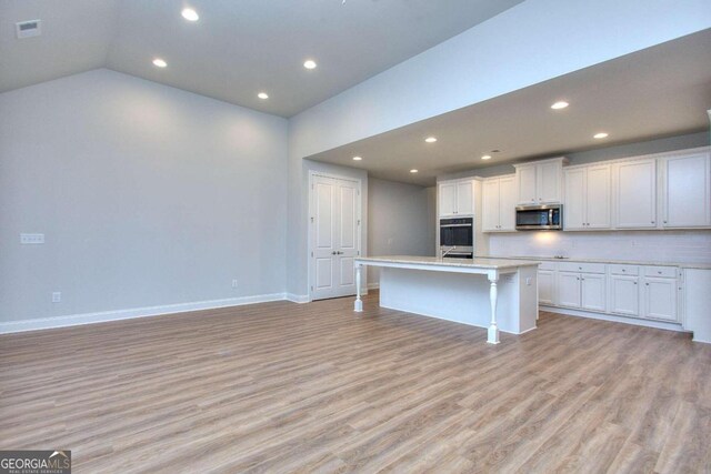 kitchen with recessed lighting, light wood-style flooring, stainless steel appliances, and a kitchen island with sink
