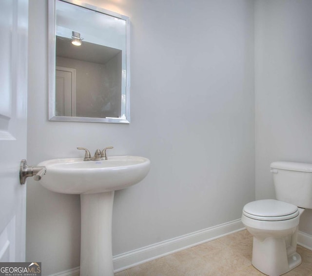 half bathroom with toilet, tile patterned flooring, a sink, and baseboards