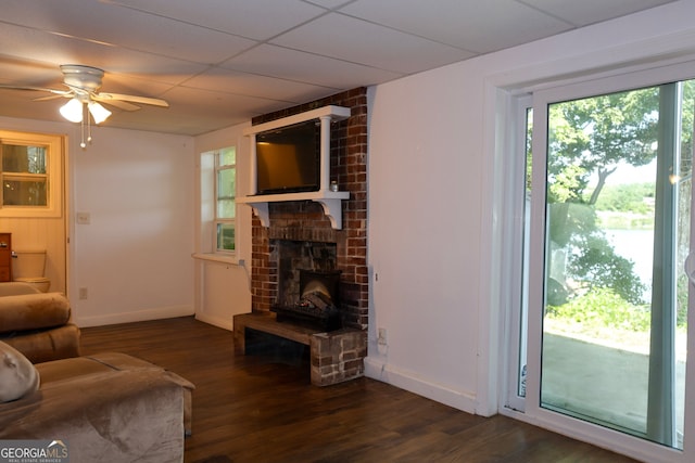 living room featuring a drop ceiling, dark hardwood / wood-style floors, a fireplace, and ceiling fan