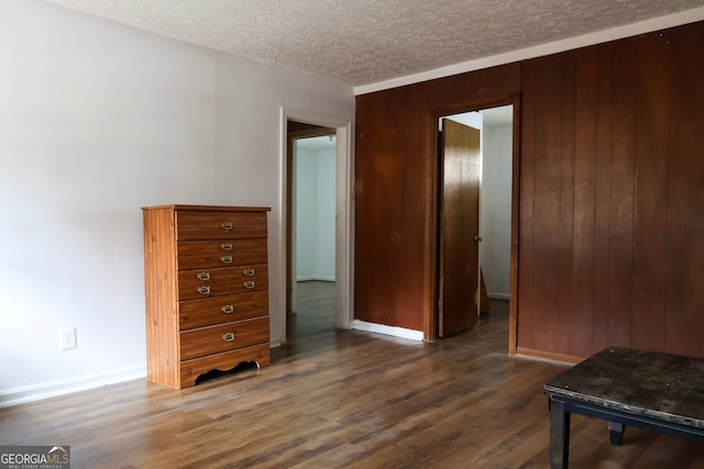 bedroom with a textured ceiling, dark hardwood / wood-style floors, and wooden walls