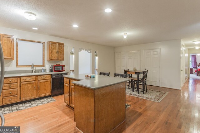 kitchen with a textured ceiling, light wood-type flooring, sink, black appliances, and a center island