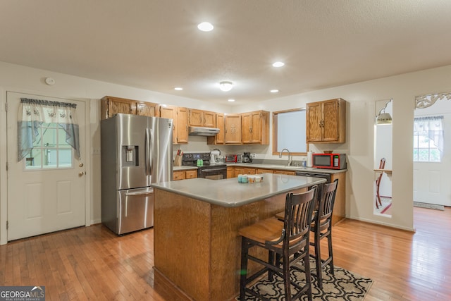 kitchen with stainless steel refrigerator with ice dispenser, a kitchen bar, black range with electric cooktop, a kitchen island, and light hardwood / wood-style flooring