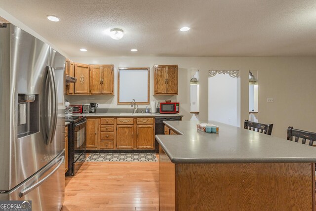 kitchen with black appliances, sink, light wood-type flooring, and a textured ceiling