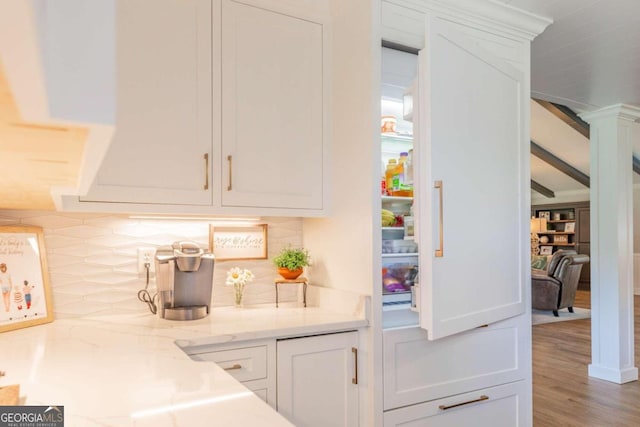 interior space featuring white cabinetry, tasteful backsplash, light stone countertops, ornate columns, and hardwood / wood-style flooring