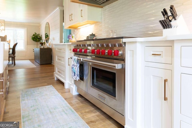 kitchen with range with two ovens, white cabinets, crown molding, light hardwood / wood-style floors, and backsplash