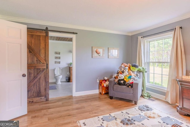 sitting room featuring light wood-type flooring, ornamental molding, a barn door, and plenty of natural light